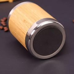 A wooden and metal coffee cup with a black rubber lid rests on a dark surface, surrounded by scattered coffee beans.