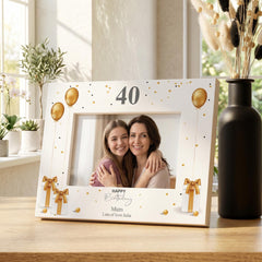 A white picture frame with a photo of two women, one older and one younger, smiling and embracing each other. The frame has gold balloons and presents a birthday celebration theme.