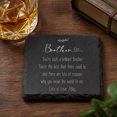 A slate coaster with a heartfelt message about a brilliant brother, accompanied by a glass of amber liquid and a book on a wooden surface.