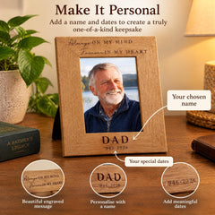 a wooden picture frame with a photo of an older man, likely a father, and a personalized message engraved on it. The frame is placed on a wooden surface, surrounded by various objects such as a potted plant, a book, and a wallet.