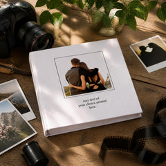 a white photo album with a printed photo of a couple embracing, surrounded by various photography equipment such as a camera, film, and other items on a wooden surface.