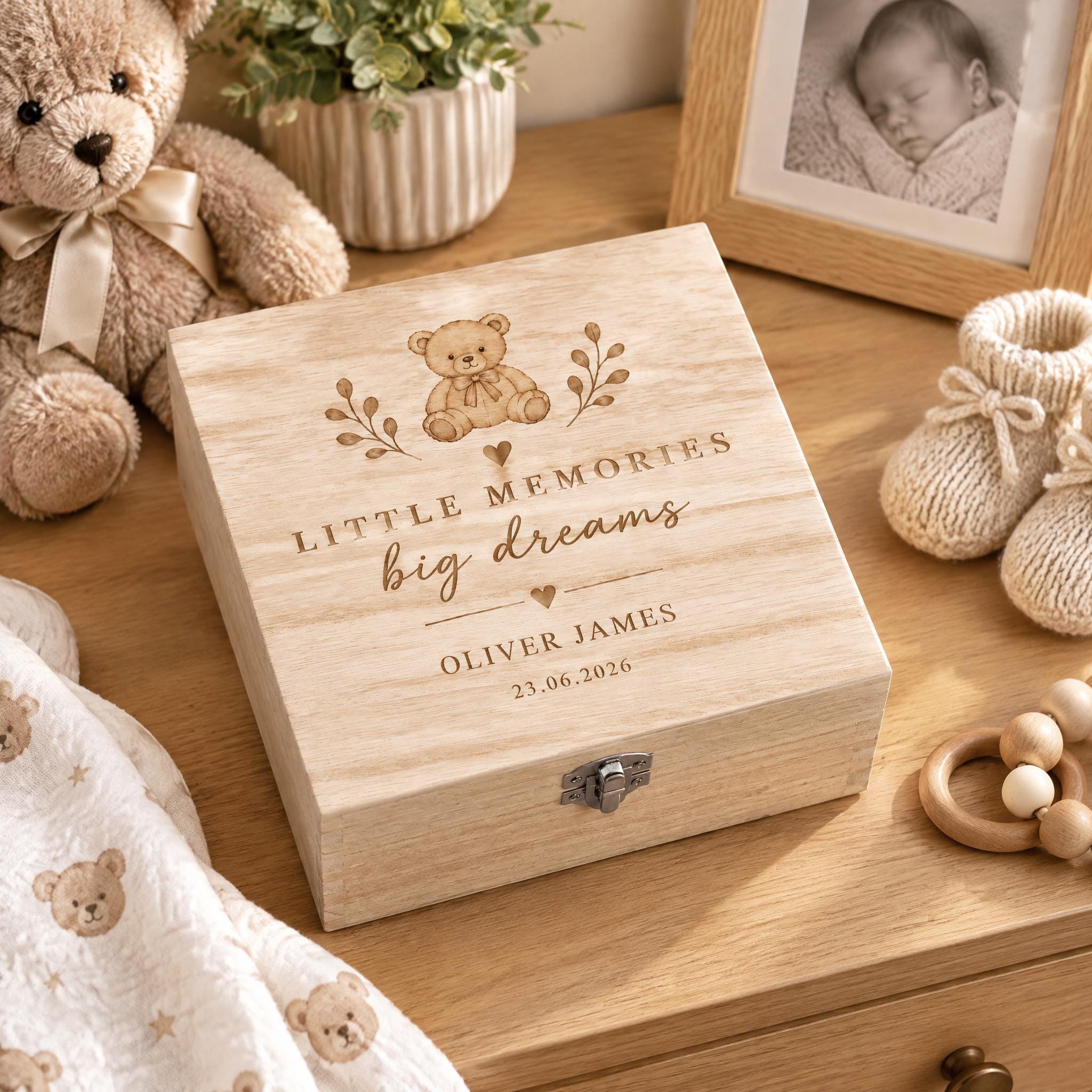 A wooden box with a teddy bear and a baby photo on it, surrounded by baby-related items such as a blanket, a toy, and a baby booties.