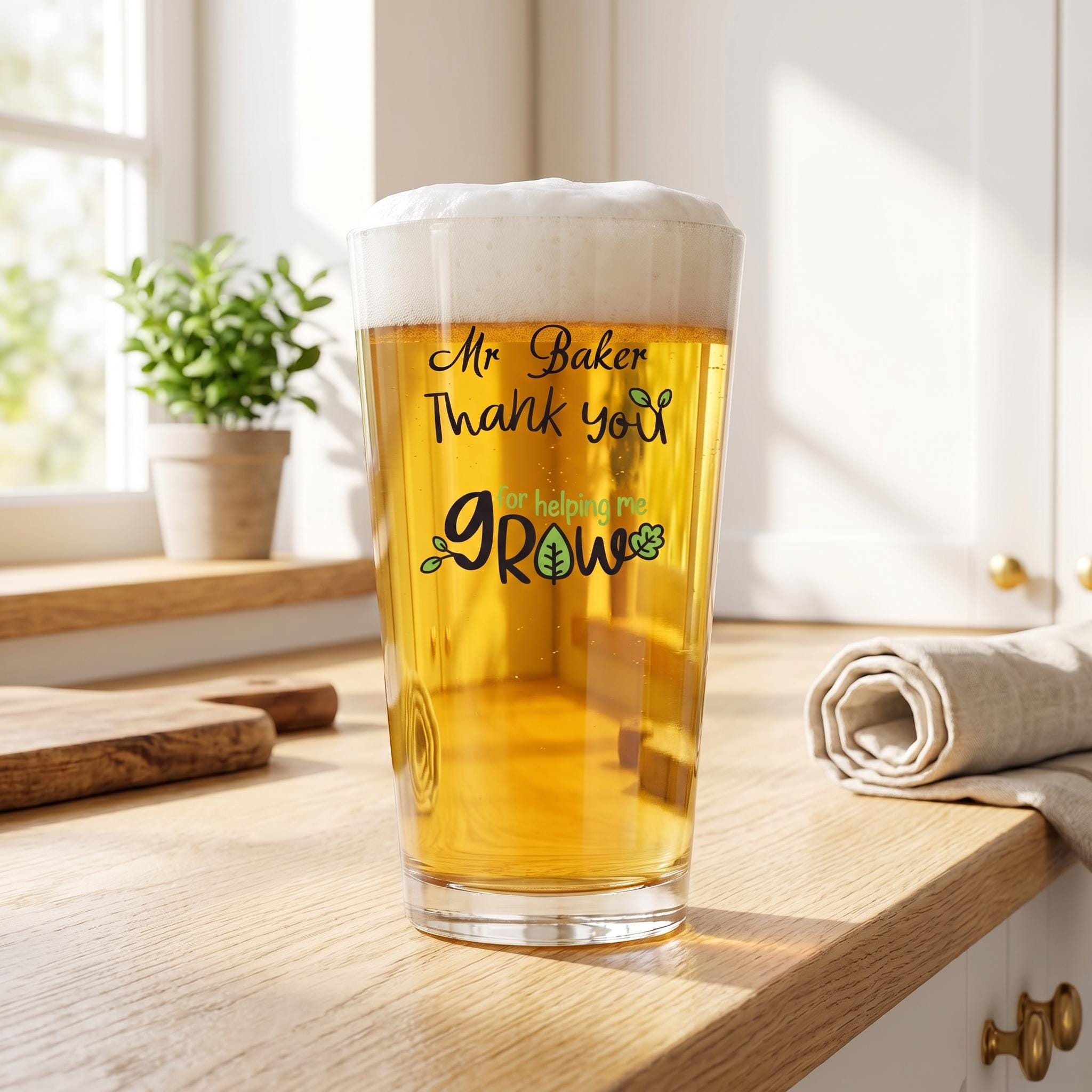 A tall glass of beer with a message printed on it, sitting on a wooden countertop next to a potted plant.