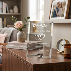 A glass frame with a personalized message on it, placed on a wooden table. The frame has a rose in a vase and a candle nearby.