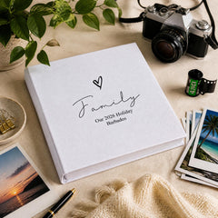 a white photo album with the word "Family" written on it, surrounded by various items such as a camera, film rolls, and a plant.