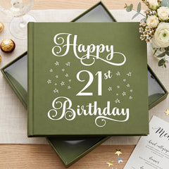 a green book with the text "Happy 21st Birthday" printed on it, placed on a table with a glass of wine, flowers, and a menu.