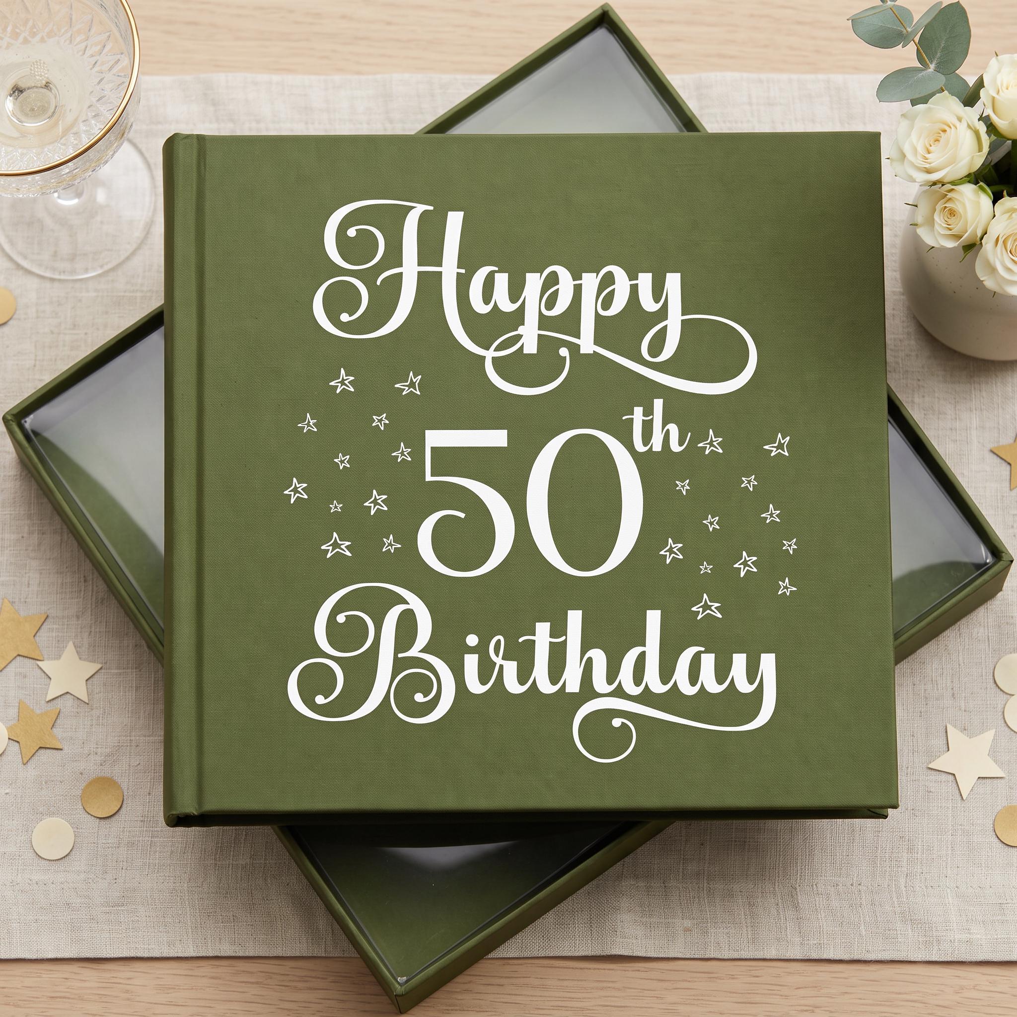 A green photo album with the text "Happy 50th Birthday" printed on it, placed on a table with a glass of wine and a bouquet of flowers.