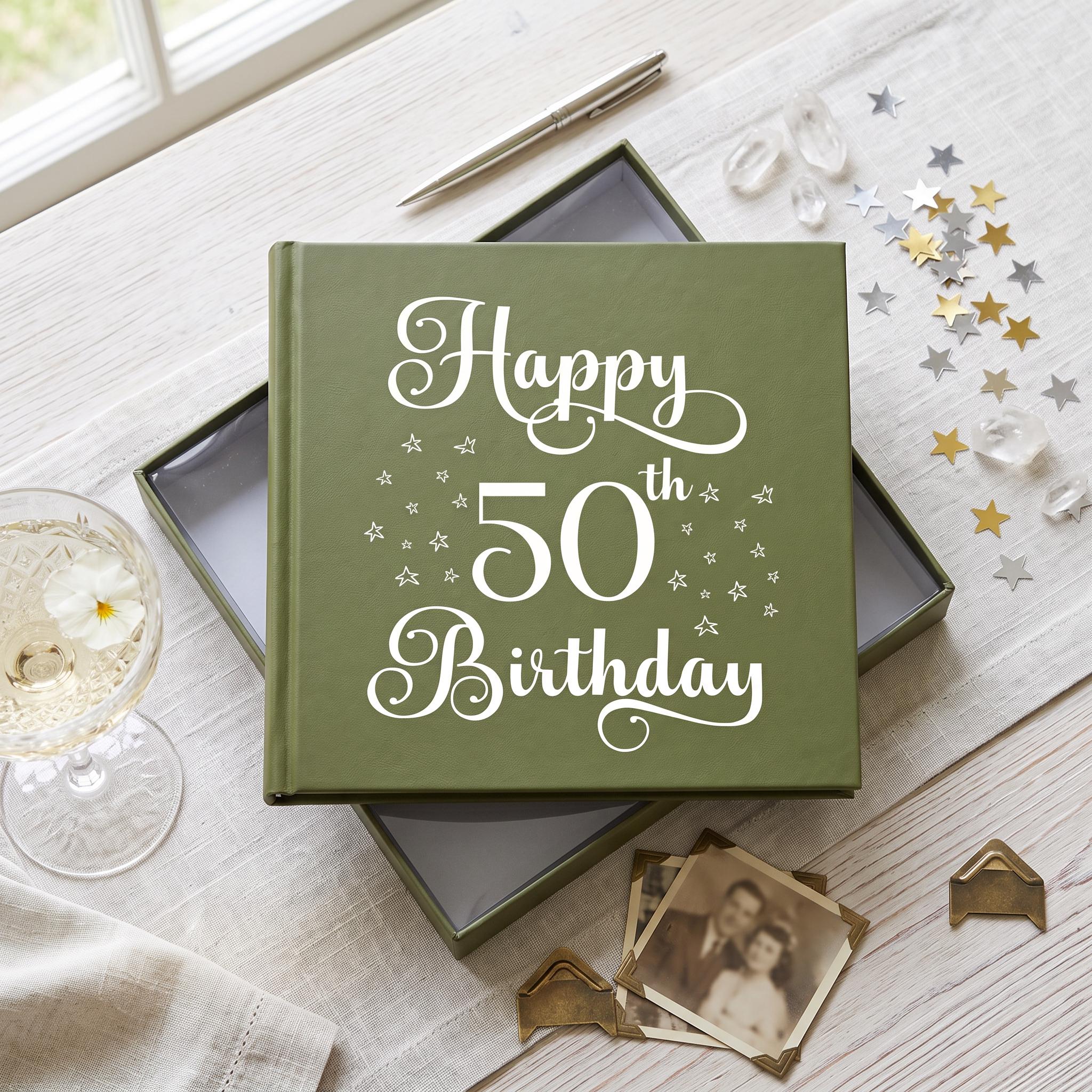 A green book titled "Happy 50th Birthday" sits on a table, surrounded by a glass of champagne, a pen, and some small star-shaped decorations.