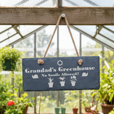 Greenhouse filled with potted plants and a sign reading 'Grandad's Greenhouse No Snails Allowed'.