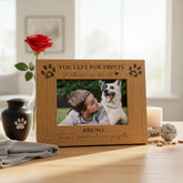 Wooden photo frame with a picture of a boy and a dog, placed on a surface with a rose and other items.