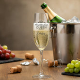 Prosecco glass with 'Prosecco Queen Emily' text, bottle, and grapes on a wooden table.