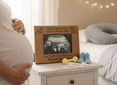 Pregnant belly with a wooden frame displaying an ultrasound, baby booties, and toys on a nightstand.