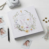 Personalized photo album with floral design on a white surface with photos and a camera.
