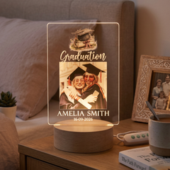 a lighted picture frame on a wooden table, displaying a graduation photo of two women wearing caps and gowns.
