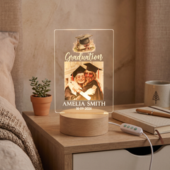 a wooden nightstand with a potted plant, a graduation photo, and a lamp.