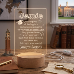 a wooden desk with various items on it, including a lighted sign that says "Wishing you all the happiness and success you deserve on your graduation day. May you embrace every opportunity, learn from every experience, and never stop believing in your potential. Congratulations!" The desk also has a small clock, a magnifying glass, and some books.