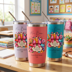 Three colorful tumblers with personalized messages, placed on a wooden desk in a classroom setting.