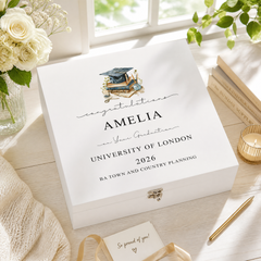 a graduation gift box with a personalized message for a graduate named Amelia, placed on a wooden surface next to a vase of white roses and a candle.