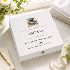 a white graduation box with a graduation cap and mortarboard, placed on a table with a vase of flowers and some books.