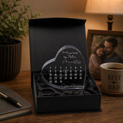 a heart-shaped calendar with a personal message, placed on a wooden desk next to a mug and a plant.