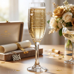 a champagne glass with a personalized message, a graduation cap, and a bouquet of flowers on a table.