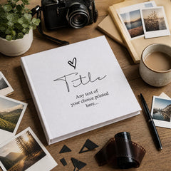 a white book with a heart symbol and the text "Title" printed on it, surrounded by various photography equipment and items such as a camera, film roll, and a cup of coffee.