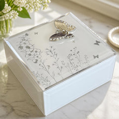 A decorative white box with a clear lid, featuring a silver butterfly design and floral patterns.