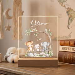 A wooden nightstand with a clear glass display case containing a picture of three cartoon animals, including a lion, a bear, and an elephant, sitting on a swing. The display case has the name "Oliver" written on it.