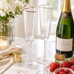 a table setting with a bottle of champagne, two champagne flutes, a plate of strawberries, and a candle.