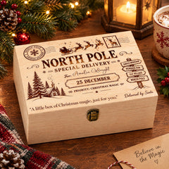 A wooden box with a Christmas-themed design, featuring a Santa Claus sleigh, pine trees, and holiday decorations, sits on a wooden surface.