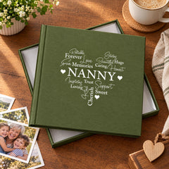 a green photo album with the word "NANNY" printed on it, sitting on a wooden surface alongside some photos and a coffee cup.