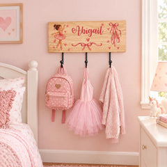 A pink-themed bedroom with a wooden coat rack displaying a ballet tutu, pink backpack, and pink sweater.