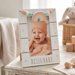 A wooden frame with a photo of a smiling baby inside, sitting on a table with a wooden toy and a stuffed animal in the background.