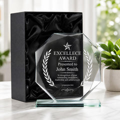 a clear glass award plaque with a black box underneath it, placed on a table.
