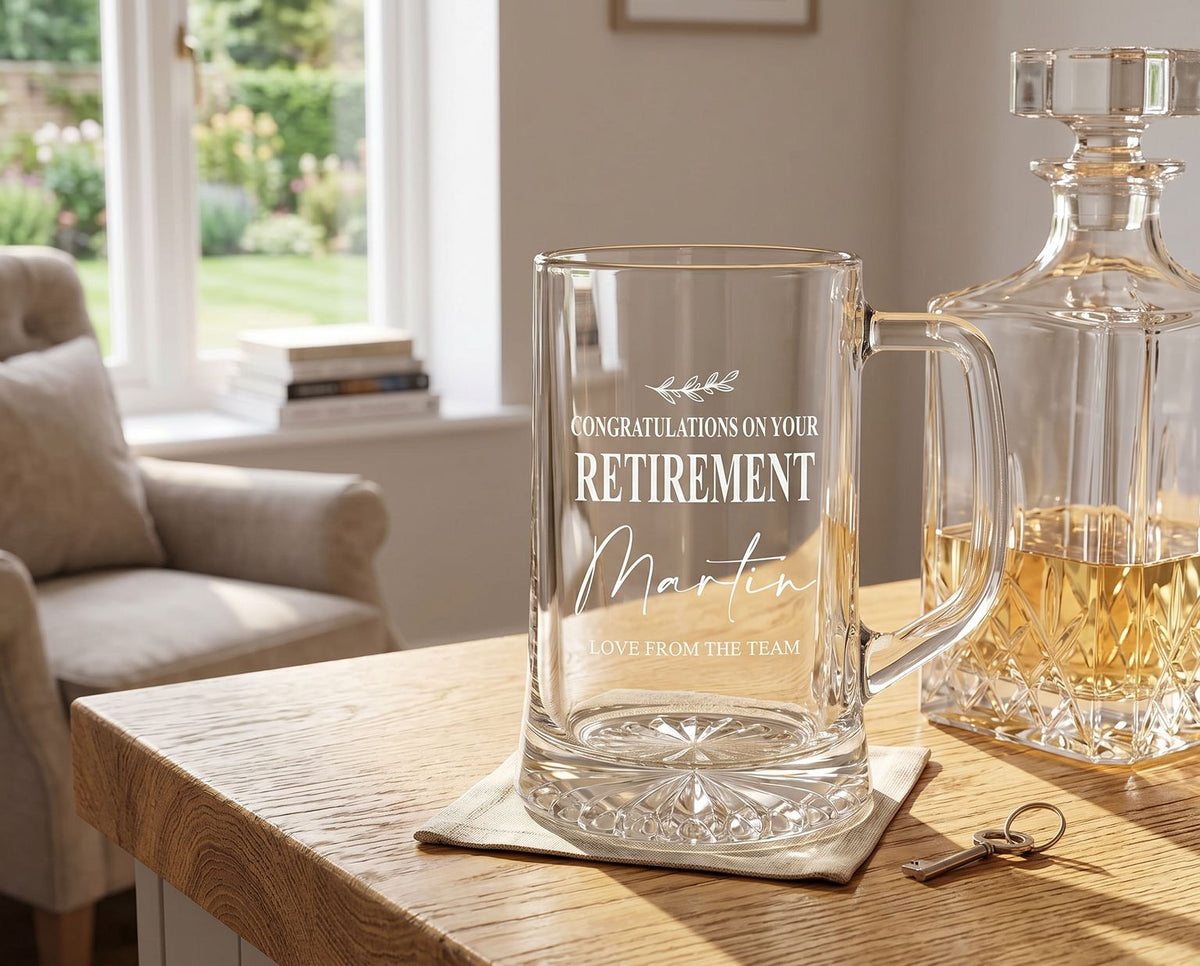 a glass mug with a personalized message on it, placed on a wooden table next to a bottle of alcohol.