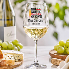 a wine glass with a personalized message, a bottle of wine, and some cheese and grapes on a table.