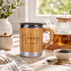A wooden mug with the name "Nanny" and the name "Love Jamieie" printed on it, sitting on a table next to a teapot and a bowl of tea leaves.