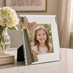A young girl with a bright smile is captured in a framed photo, placed on a table next to a vase of white flowers and a book.
