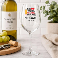 a wine glass with a personalized message, a bottle of Sauvignon Blanc, and some grapes on a table.
