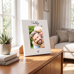 A white picture frame with a photo of a smiling man and a young boy, placed on a wooden table in a living room.