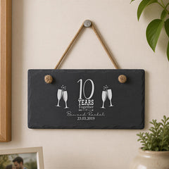 A black slate sign with white text and graphics hangs on a wall, celebrating a 10-year anniversary.