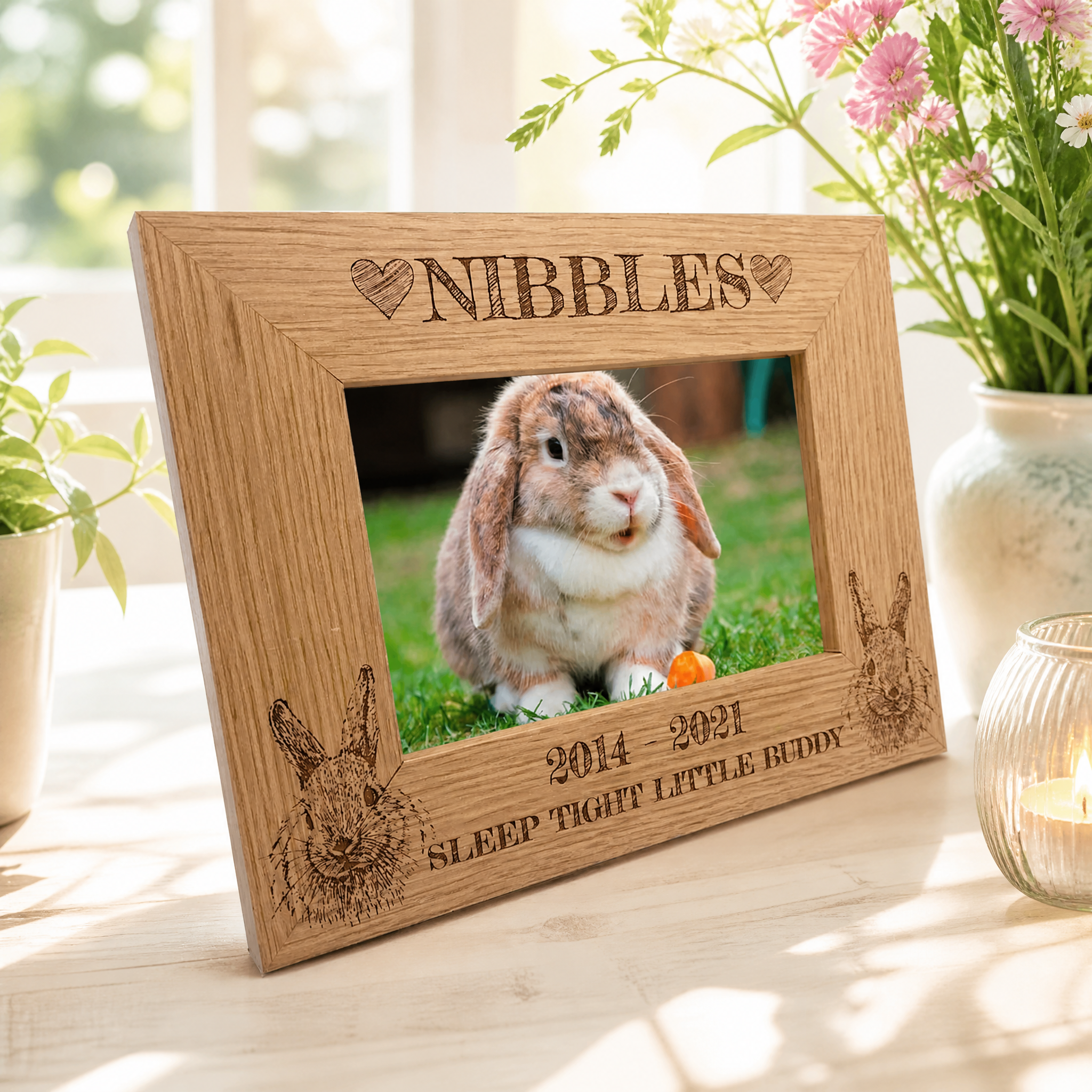 A wooden picture frame with a photo of a rabbit inside, surrounded by decorative elements such as a vase of flowers and a candle.