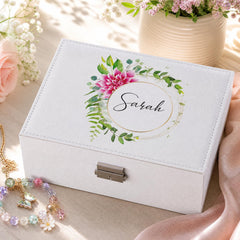A white jewelry box with a floral design and the name "Sarah" printed on it, placed on a wooden surface next to a vase of pink flowers and a necklace.
