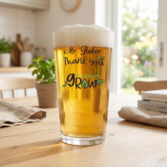 A tall glass of beer with a message on it, sitting on a wooden table in a kitchen.