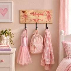 A pink-themed bedroom with a wooden coat rack displaying a ballet tutu, a backpack, and a pink towel.