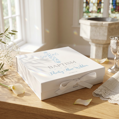 A white box with a blue floral design and the text "Baptism" sits on a wooden table, accompanied by a silver chalice and a white lace doily.