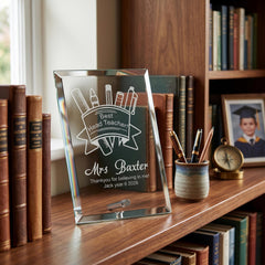 A glass trophy with a personalized message, placed on a bookshelf next to a picture frame and a cup of pens.
