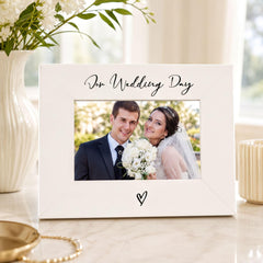 A white picture frame with a photo of a bride and groom inside, placed on a marble surface.