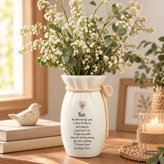 A white vase with a personalized message, a small bird figurine, and a candle on a wooden table.