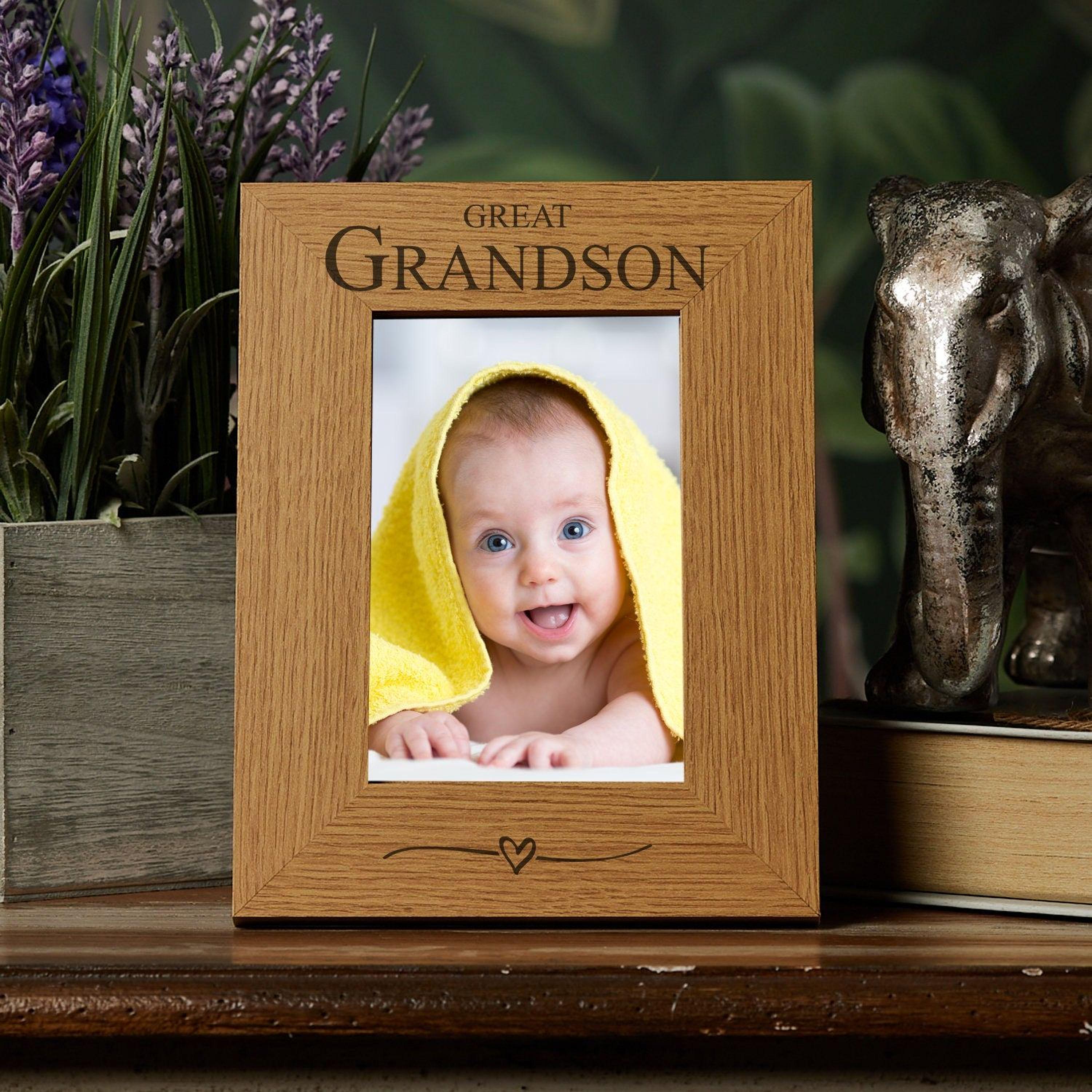 A wooden picture frame with a photo of a smiling baby wrapped in a yellow towel, placed on a wooden surface next to a metal elephant figurine.